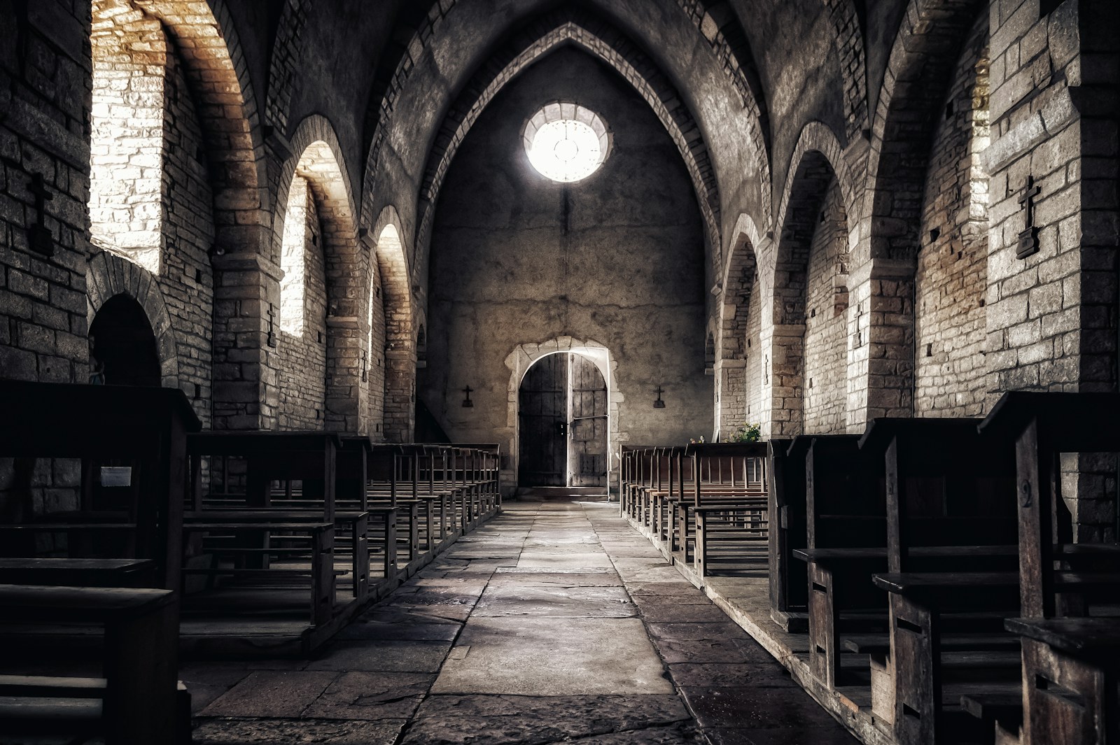 An empty church interior with rows of wooden pews and warm sunlight streaming through a bright window, no people visible.