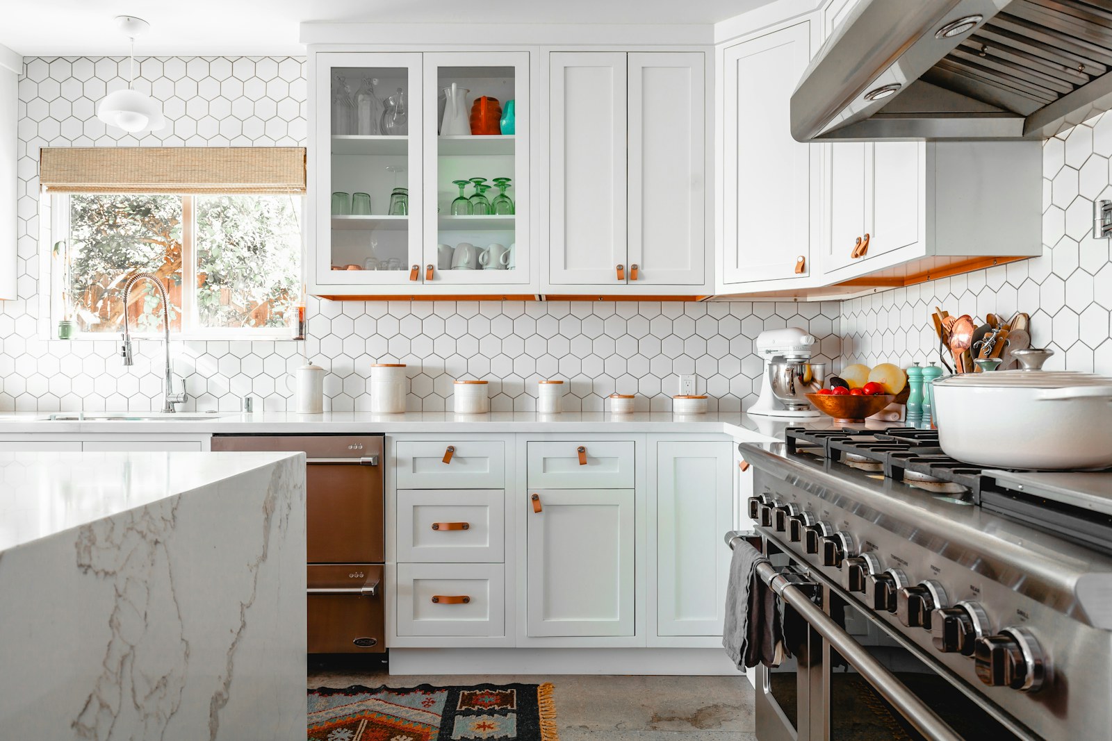 A bright, spotless modern kitchen with white cabinetry, hexagonal tile backsplash, a marble island, and stainless steel range.