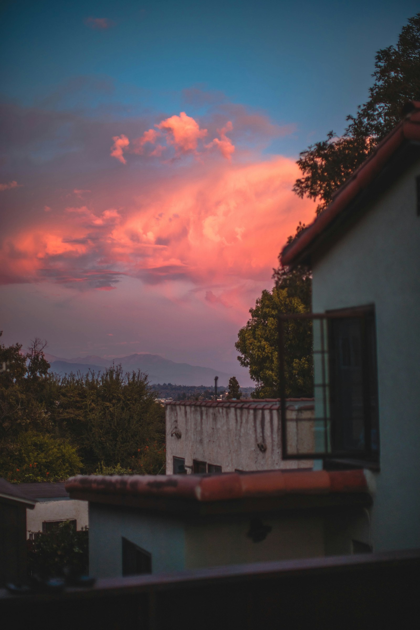 A residential house roofline silhouetted against a dramatic pink and orange sunset sky.