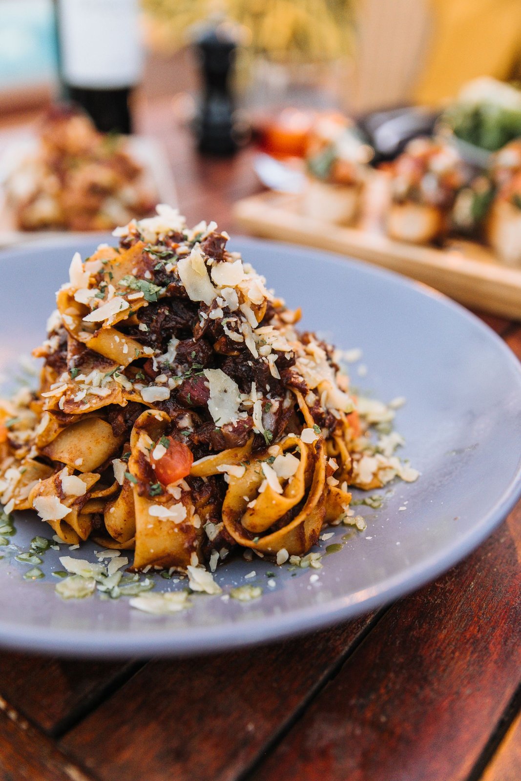 A nest of ribbon pasta with sauce, herbs and shaved cheese on a blue plate in a restaurant.