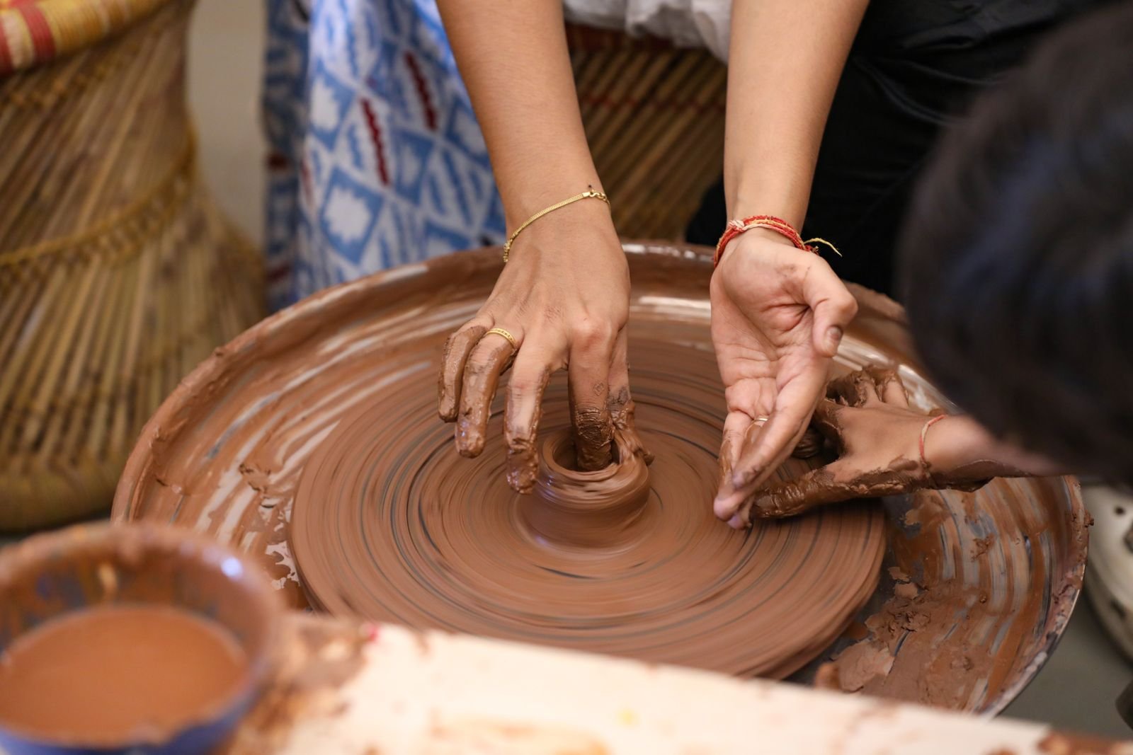 Hands shaping wet clay on a spinning pottery wheel during a group workshop.