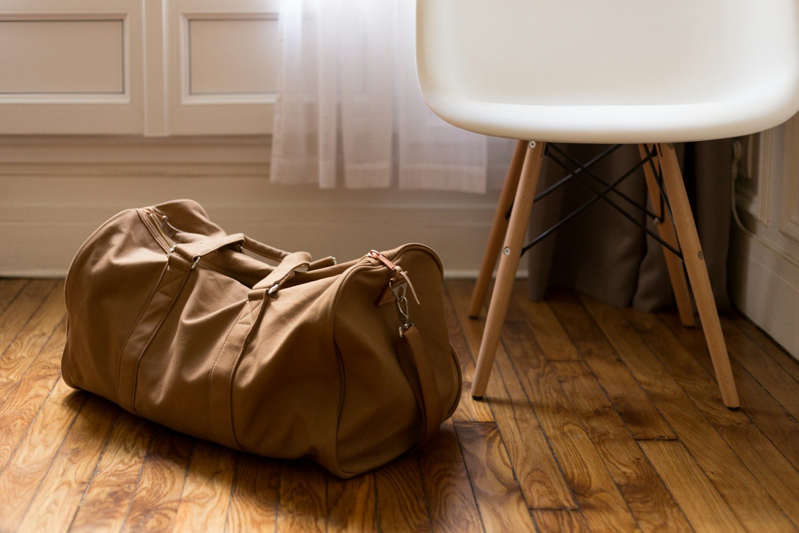 Tan canvas and leather duffel bag beside a chair.