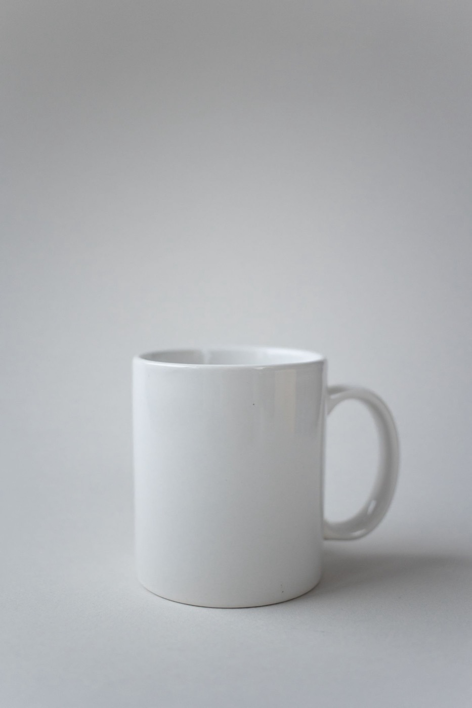A plain white ceramic mug with a rounded handle on a light gray surface.