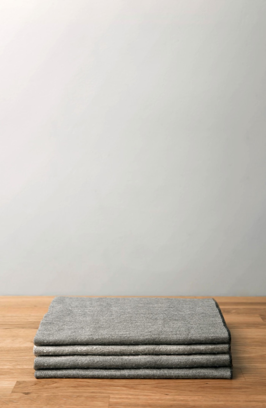 A neatly folded gray throw on a wooden surface against a pale wall.