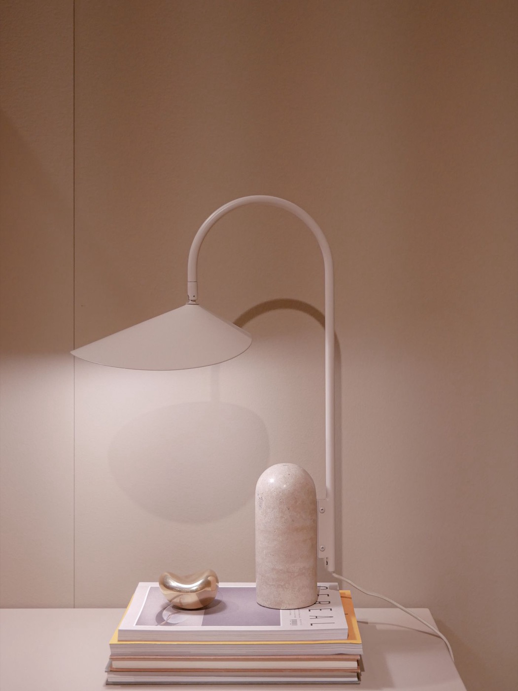 A white arched table lamp with a conical shade and stone cylinder base, styled on books.