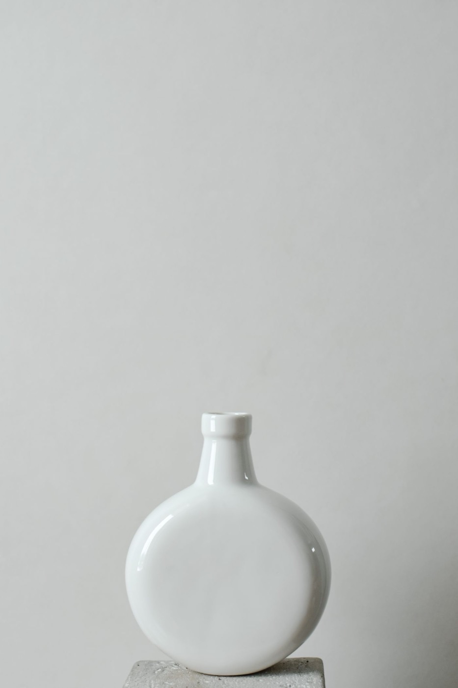A glossy white ceramic bottle vase on a stone pedestal.